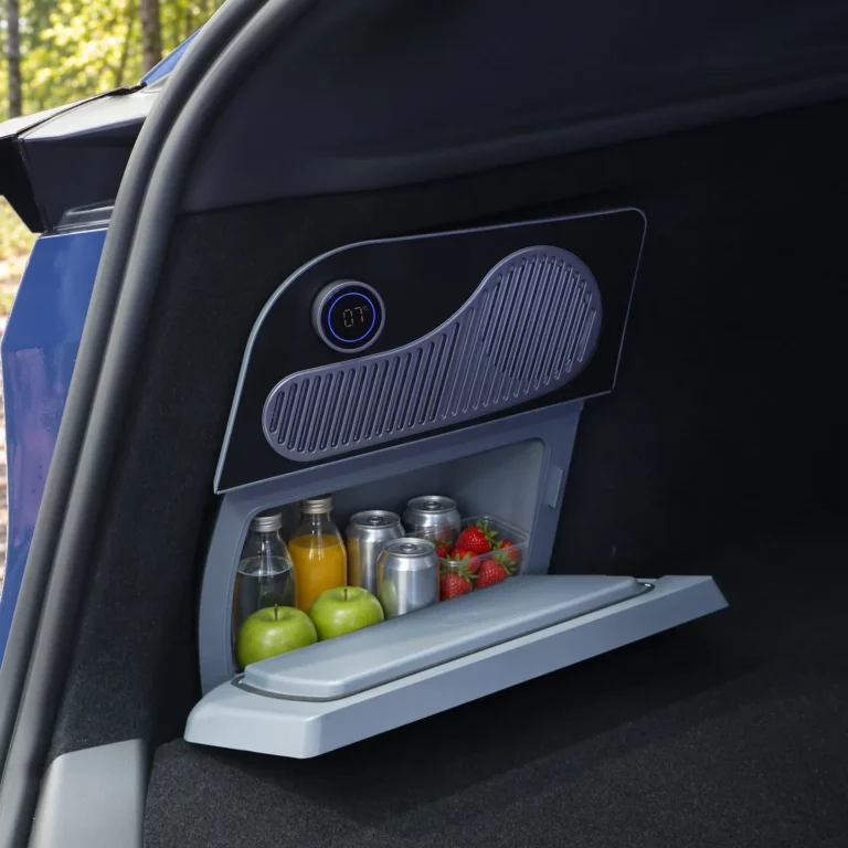 Glacière électrique à façade noire intégrée au rangement gauche du coffre d’une Tesla Model Y, porte abaissée à l’horizontale, bac gris garni de boissons et de fruits