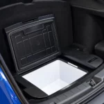 Glacière électrique ouverte, cuve blanche et couvercle noir, dans le sous-coffre d’une Tesla Model Y bleue