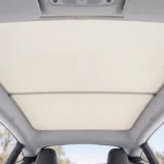 Pare-soleil beige posé sous le toit vitré d’une Tesla Model Y, vu depuis les sièges avant