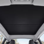 Pare-soleil noir posé sous le toit vitré d’une Tesla Model Y, vu depuis les sièges avant