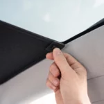 Une main glisse un clip du pare-soleil entre le toit vitré et le ciel de toit d’une Tesla Model Y